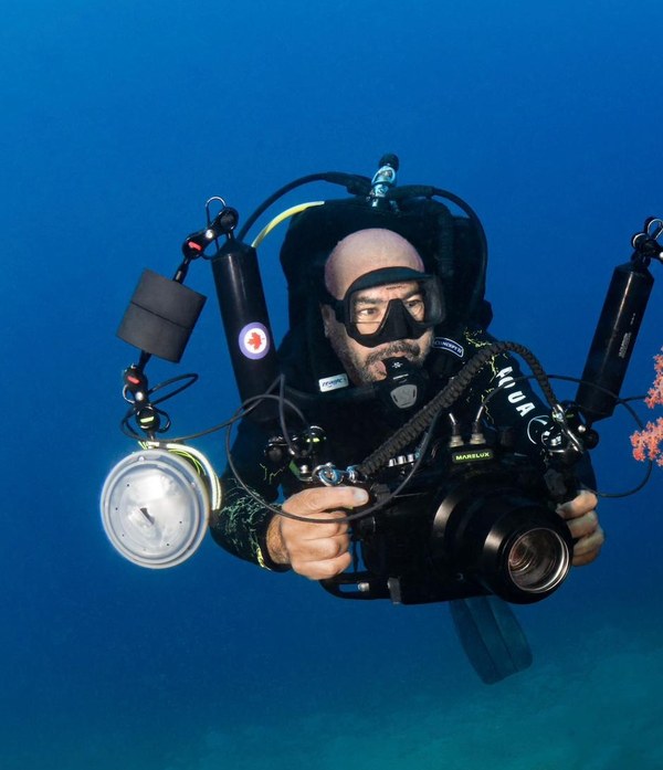 Yazan Alsaed, founder and PADI instructor at Sea Guard, diving with an underwater camera beside a reef